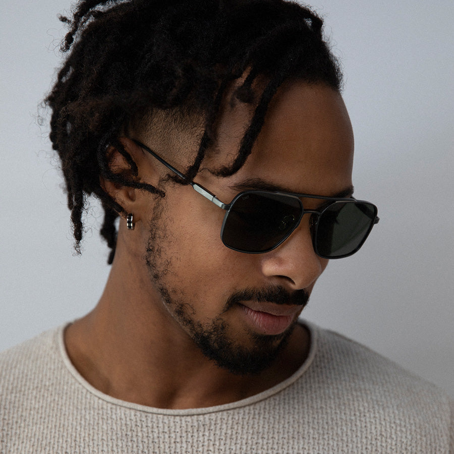 Black man wearing large square metal sunglasseslooking down