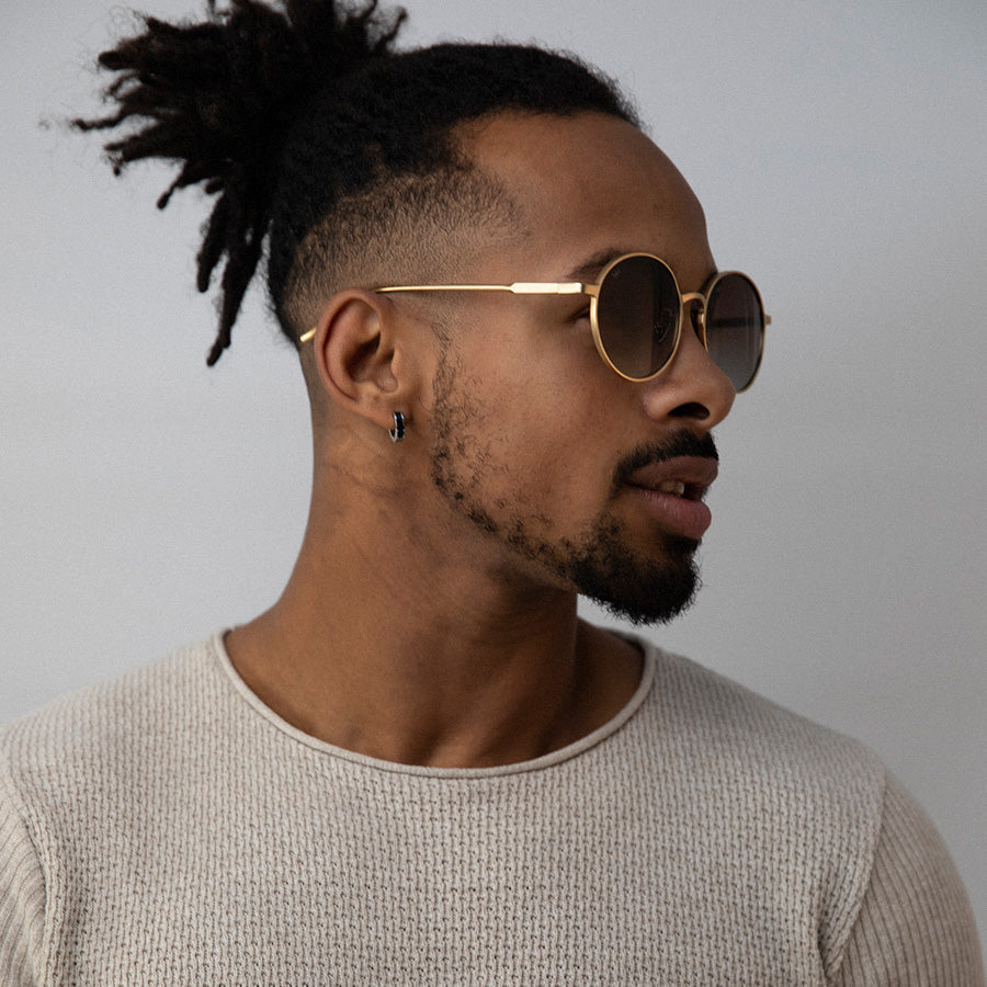 Black man wearinground sunglasses with gold frame and grey lenses looking sideways